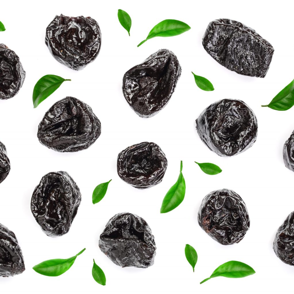 Dried Plum Prunes Decorated With Green Leaves Isolated On A White Background. Top View. Flat Lay